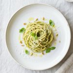 An overhead, photorealistic flat lay of an elegantly presented meal, exemplifying sophisticated simplicity. Fresh, vibrant ingredients, like a crisp salad or minimalist pasta, are artfully arranged on a clean white plate with delicate garnishes and a light sauce. Bright, natural lighting highlights the appealing textures against a minimalist background, creating an inspiring, clean aesthetic.