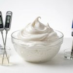 A clean, photorealistic studio shot featuring a perfectly stable aquafaba meringue in a clear glass bowl, surrounded by a precision digital scale, thermometer, and pH meter with visible numerical readouts, conveying scientific rigor in vegan baking.