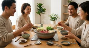 An ultra-photorealistic, high-detail image of a serene communal dining experience. At the center, a gently steaming Japanese donabe pot, filled with Wagyu, fresh vegetables, and udon, rests on a modern wood table with an integrated cooktop. Around the table, three to four adults mindfully use chopsticks, smiling and conversing in soft, natural daylight, conveying a sense of shared well-being.