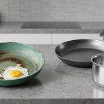 A still-life on a modern kitchen counter features a badly degraded green ceramic non-stick frying pan with a stuck fried egg. In stark contrast, a pristine dark gray carbon steel frying pan and a gleaming stainless steel saucepan are displayed, highlighting durable alternatives to the failed ceramic cookware.