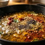 A photorealistic close-up of vibrant whole and ground spices, like turmeric and cumin, gently sizzling and blooming in shimmering golden oil in a pan, with small bubbles visible.