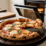 Photorealistic close-up of a steaming, perfectly baked Neapolitan pizza on a dark carbon steel plate. A hand lifts a firm slice with a metal spatula, revealing melted mozzarella, vibrant red sauce, and fresh basil, set in a softly blurred modern kitchen.