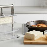 A photorealistic studio image detailing the preparation of tofu: a modern press expels water from raw tofu, a dense block absorbs golden marinade, and perfectly seared, golden-brown tofu steams in a hot cast-iron skillet.