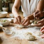A close-up of diverse hands expertly folding perfectly formed, raw dumplings on a clean wooden counter. Bathed in soft, warm natural light, neatly arranged ingredients surround the collaborative activity, evoking calm, joyful communal cooking.