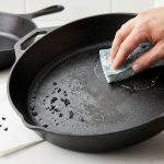 A photorealistic image depicting cast iron skillet care: a close-up of a skillet with flaking seasoning and flakes on a white counter, a hand scrubbing another skillet with soap, and a perfectly seasoned skillet in the background of a clean kitchen.