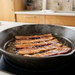A photorealistic image of thick-cut bacon strips perfectly laid in a pristine pan, gently frying with subtle steam and golden-brown edges, in a bright, clean kitchen setting.