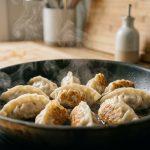 A close-up shows plump, perfectly sealed homemade dumplings, golden-brown and crispy on the bottom, gently steaming in a clean pan. The blurred modern kitchen background and warm natural light evoke culinary satisfaction.