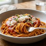 A close-up, photorealistic image of a perfectly prepared bowl of pasta in a simple ceramic bowl. A fork gently twirls a portion, showcasing the rich, creamy sauce flawlessly coating every al dente noodle, garnished with grated cheese and fresh herbs.