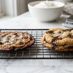 Side-by-side comparison of two chocolate chip cookies on a wire cooling rack. The left cookie is flat, thin, and greasy with dark edges, while the right cookie is thick, golden-brown, and soft, topped with melted chocolate pools and flaky sea salt.