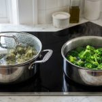 **Alt text:** Side-by-side comparison of cooking broccoli in two pots on a modern stovetop. The left pot, covered with a foggy glass lid, contains dull, overcooked grey-green broccoli. The right, open pot contains vibrant, bright green broccoli with a gentle wisp of steam rising.