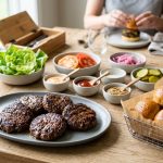 **Alt text:** A bright, gourmet build-your-own slider station on a light oak table, featuring juicy grilled beef patties, mini brioche buns, and bowls of fresh toppings in a soft, natural daylight setting.