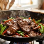 **Alt text:** An extreme close-up of sizzling beef stir-fry in a wok, featuring glistening, tender slices of glazed beef, vibrant green snap peas, and red bell peppers with wisps of steam rising.