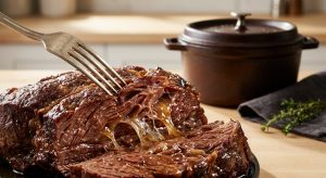 **Alt text:** An extreme close-up of a silver fork pulling apart a tender beef chuck roast, revealing glistening, juicy muscle fibers and melted gelatin under warm light, with a blurred Dutch oven in the background.