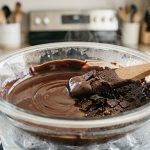 **Alt text:** Macro shot of dark chocolate in a glass bowl, contrasting smooth, glossy melted chocolate on one side with stiff, dry, and clumpy seized chocolate on the other, highlighted by a wooden spatula.
