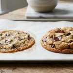 A side-by-side comparison of two chocolate chip cookies on a baking sheet. The left cookie is flat, thin, and greasy with overly spread edges. The right cookie is thick, perfectly domed, and golden-brown with pools of melted dark chocolate.